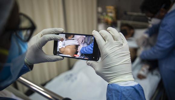 Un médico revisa a un paciente con llagas causadas por una infección de viruela del simio mientras otro toma una fotografía, en el área de aislamiento para pacientes con viruela del simio en el hospital Arzobispo Loayza, en Lima, el 16 de agosto de 2022. (Foto: Ernesto BENAVIDES / AFP)