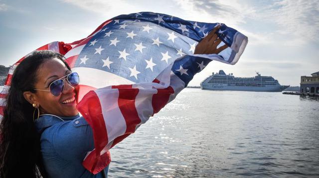 Una mujer agita una bandera cubana al paso del barco Adonia de Fathom, filial de la empresa estadounidense Carnival, que atracó en el puerto de La Habana con 700 pasajeros a bordo tras haber partido de Miami la tarde del domingo. (Foto: AFP)
