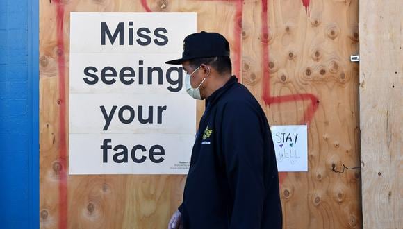 Un hombre con una máscara facial por el coronavirus camina junto a un letrero publicado en un restaurante tapiado en San Francisco, California. (Foto: AFP/Josh Edelson)