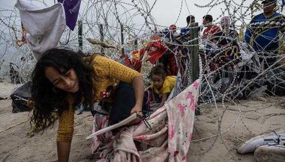 Migrantes se arrastran para cruzar a través de un agujero en el alambre de púas en Texas (Foto de ANDREW CABALLERO-REYNOLDS / AFP).