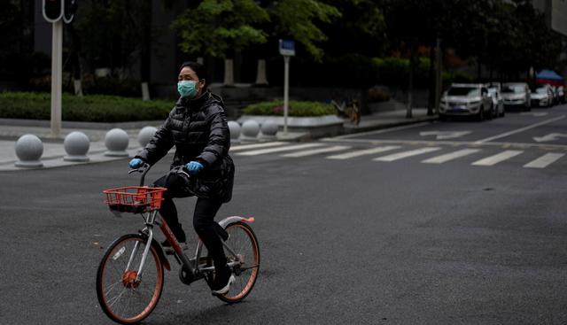 Una mujer con una máscara facial es vista en bicicleta este 28 de marzo de 2020 por una calle de Wuhan, provincia central de Hubei de China. (AFP)