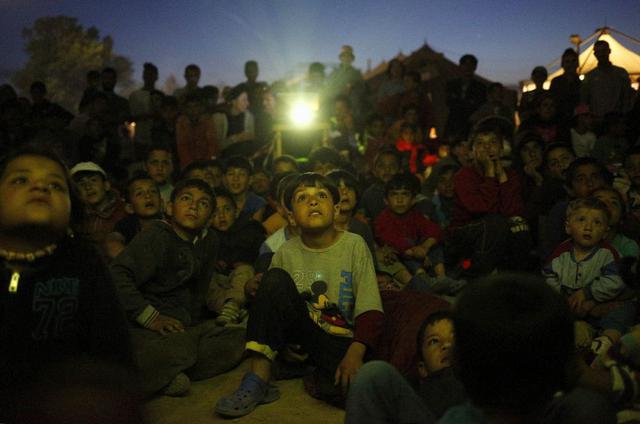 Un grupo de chicos ven una película de dibujos animados. Una proyección en un campamento improvisado de inmigrantes y refugiados que se encuentra en la frontera entre Grecia y Macedonia, cerca de Idomeni. (Foto Reuters)