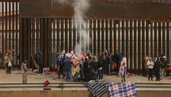 Migrantes que buscan asilo en Estados Unidos se paran alrededor de una fogata para calentarse después de cruzar el Río Grande desde Ciudad Juárez en Chihuahua, México, el 2 de enero de 2023. (Foto de HERIKA MARTINEZ / AFP)