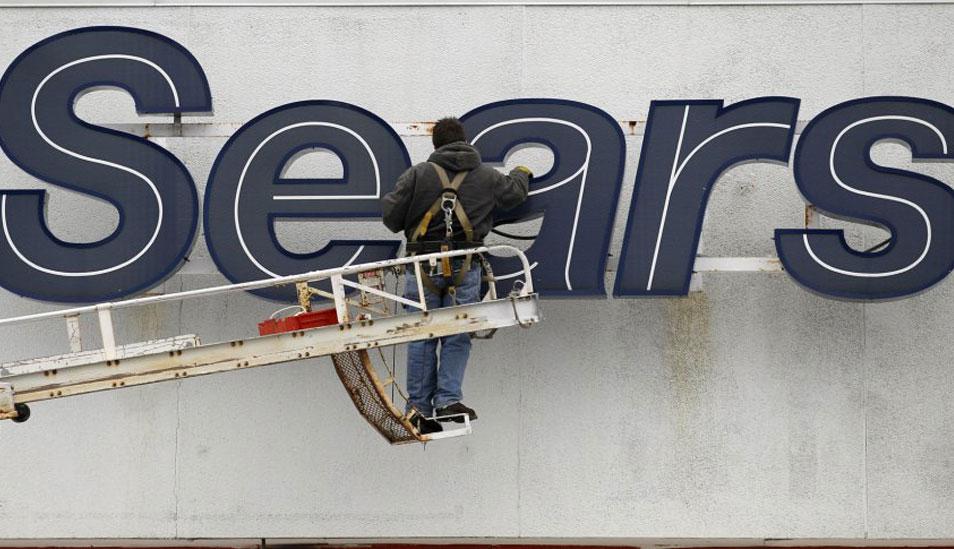 FOTO 8 | El grupo llegó a tener 355.000 empleados y 3.800 locales en Norteamérica. En la imagen, un empleado repara el logotipo de la compañía en la fachada de unos grandes almacenes de Sears en Solon, Ohio (EE UU), en 2012. (Foto: AP/ EL PAÍS)