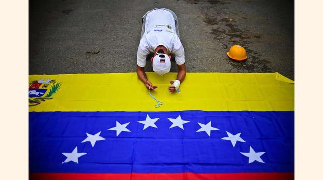 Un opositor reza sobre una bandera nacional durante una marcha contra Maduro el 1 de mayo de 2017 en Caracas.(foto: Ronaldo Schemidt).