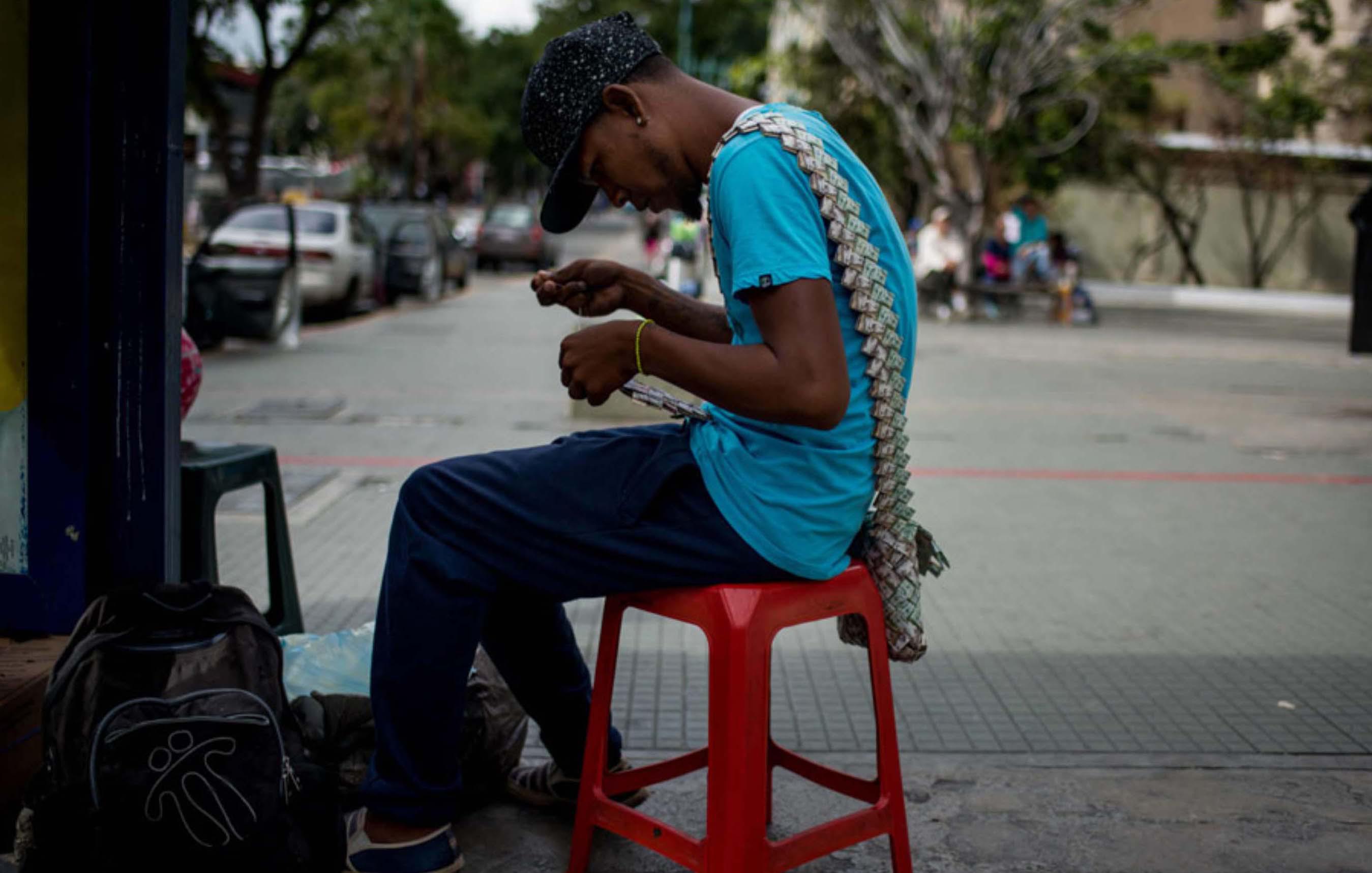 FOTO 1 | 1. El vendedor Wilmer Rojas (25) decidió incursionar en el arte callejero. Comenzó realizando pequeños barcos con los billetes que se encontraba tirados en el piso de las principales avenidas. En 2017, la inflación llegó hasta un 2.600% en Venezuela.  (Foto: AFP)