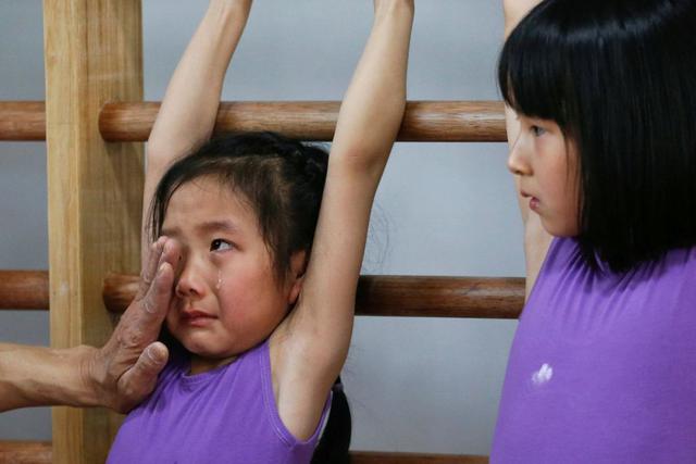 El entrenador de esta niña le limpia las lágrimas y le consuela cuando se sentía cansada a mitad de las clases de gimnasia en la Escuela de Atletismo Yangpu en Shanghai, China. (Foto Reuters)