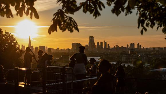 Los peatones observan la puesta de sol sobre los rascacielos en el horizonte desde Greenwich Park en Londres, Reino Unido, el jueves 30 de julio de 2020.