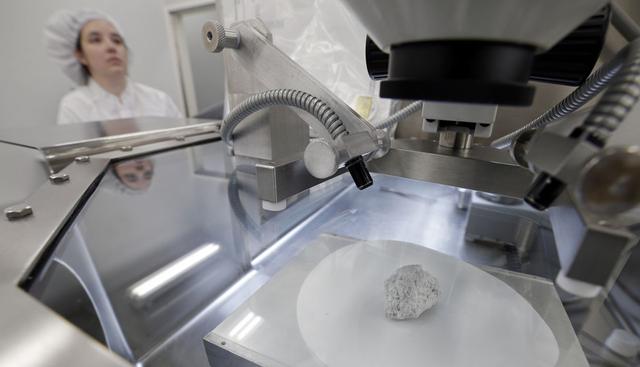 FOTO 11 | muestras de roca lunar selladas desde las misiones Apolo
En primer plano, la conocida como roca génesis, una roca anortosita de 4 400 millones de antigüedad que mide 2 pulgadas de largo, fue recuperada por la misión Apolo 15 y fue usada para determinar que la Luna se formó por un impacto gigantesco, colocada dentro de una caja de vidrio presurizada con nitrógeno para su análisis. Lacey Costello, curadora de las muestras de las misiones Apolo, trabaja con otras muestras fuera de la caja en el laboratorio lunar del Centro Espacial Johnson de la NASA en Houston en una foto del 17 de junio de 2019 (Foto: Michael Wyke / AP).