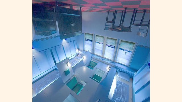 Patas arriba – Propeller Island City Lodge (Berlín, Alemania). ¿Dónde duerme uno cuando la cama cuelga del techo junto al resto del mobiliario? Pues en unos compartimentos ocultos en el suelo/techo y que más que camas parecen… ataúdes.