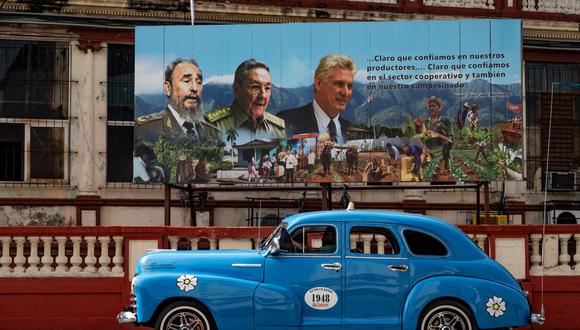 Un viejo automóvil estadounidense pasa cerca de un cartel del difunto líder cubano Fidel Castro, el ex presidente Raúl Castro y el actual presidente Miguel Díaz-Canel en La Habana, el 17 de agosto de 2023. (Foto de YAMIL LAGE / AFP).