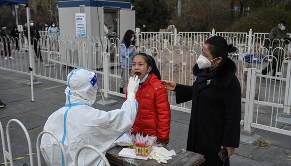 Un trabajador de la salud toma una muestra de hisopo de una niña para hacerle la prueba del coronavirus en una estación de recolección en Beijing el 22 de noviembre de 2022. (Foto de Jade GAO / AFP)