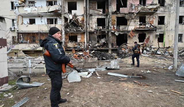 Oficiales de policía montan guardia en un edificio residencial dañado en la calle Koshytsa, un suburbio de la capital ucraniana, Kiev, donde supuestamente cayó un proyectil militar, el 25 de febrero de 2022. (Foto de GENYA SAVILOV / AFP)