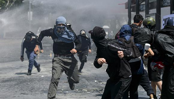 Manifestantes corren mientras chocan con antidisturbios durante una protesta para conmemorar el tercer aniversario de un levantamiento social contra el aumento de los precios de los servicios públicos, en las inmediaciones de la plaza Baquedano en Santiago, el 18 de octubre de 2022. (Foto: Martin BERNETTI / AFP)