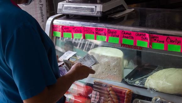 Una mujer cuenta billetes de Bolívar junto a un frigorífico de delicatessen con carteles no escritos de los precios de los productos en Caracas, Venezuela, el 28 de septiembre de 2021. (Foto: CRISTIAN HERNANDEZ / AFP)