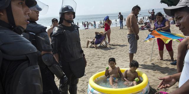 FOTO 7 | En esta imagen, tomada el 15 de febrero de 2020, dos niños dentro de una piscina hinchable comen manzanas cubiertas de azúcar mientras policías se disponen a retirar de la playa a un vendedor ambulante sin licencia, en Agua Dulce, Lima, Perú. (AP Foto/Rodrigo Abd)