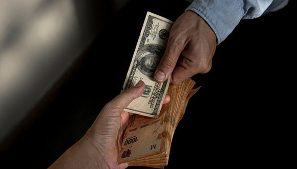 Un cambista sostiene un billete de cien dólares estadounidenses y billetes de 1,000 pesos en Buenos Aires.