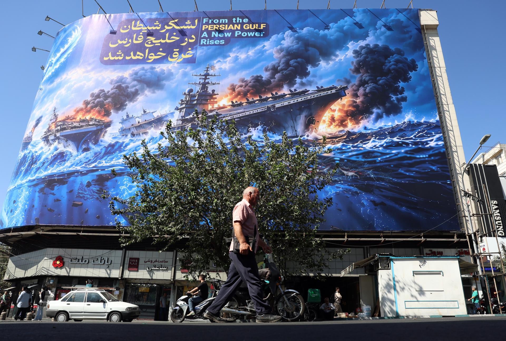 Iraníes caminan junto a una valla publicitaria anti Estados Unidos que muestra una frase en persa que dice: "El ejército del diablo se ahogará en el Golfo Pérsico", en la plaza Enghelab de Teherán, Irán, el 21 de septiembre de 2026. (EFE/EPA/ABEDIN TAHERKENAREH).