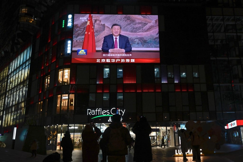 Personas bajo una gran pantalla que muestra al presidente de China, Xi Jinping, pronunciando un discurso antes de las celebraciones de Nochevieja en Pekín el 31 de diciembre de 2025. El presidente de China, Xi Jinping, declaró el 31 de diciembre que "la reunificación... es imparable" al dirigirse a la nación poco después de que el ejército de Pekín anunciara el fin de los ejercicios con fuego real en Taiwán. (Foto de WANG Zhao / AFP)