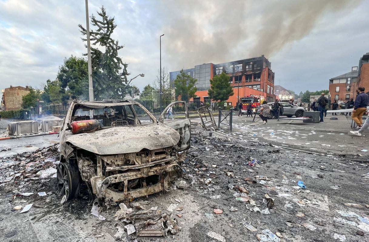 Un vehículo incendiado se encuentra en una calle frente al edificio del grupo Tessi dañado por el fuego en el distrito de Alma de Roubaix el 30 de junio de 2023, que fue completamente destruido por el fuego durante las protestas después de que un niño de 17 años recibió un disparo en el pecho. por la policía a quemarropa en Nanterre, un suburbio al oeste de París. . El edificio, que albergaba una empresa de procesamiento de datos para bancos y compañías de seguros, se incendió por completo, luego de otra noche de tensión tras la muerte del conductor adolescente en el suburbio parisino de Nanterre el 27 de junio. El presidente Emmanuel Macron se fue temprano de una cumbre de la UE. en Bruselas para regresar a Francia, donde han tenido lugar tres noches de disturbios por el tiroteo policial de un adolescente. (Foto de DENIS CHARLET / AFP)
