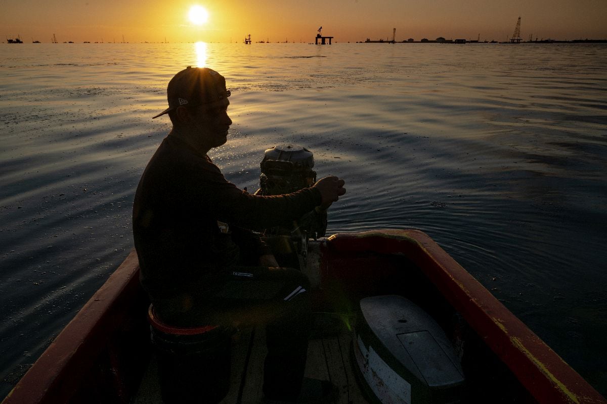 Un pescador navega por las aguas del lago Maracaibo, cubiertas de una mancha de petróleo.