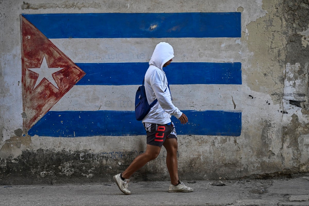 Un hombre pasa junto a un muro pintado con la bandera cubana en una calle de La Habana durante un apagón nacional, el 22 de marzo de 2026. (YAMIL LAGE / AFP)