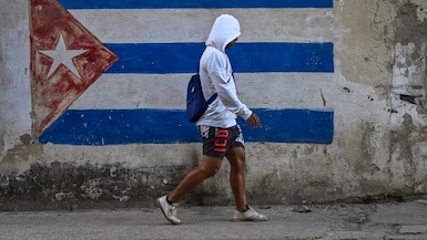 Un hombre pasa junto a un muro pintado con la bandera cubana en una calle de La Habana durante un apagón nacional, el 22 de marzo de 2026. (YAMIL LAGE / AFP)