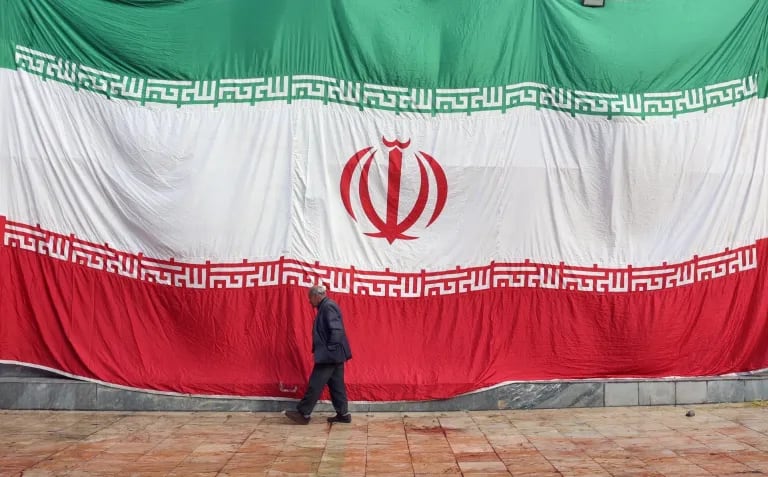 Un hombre pasa delante de una enorme bandera iraní, en una imagen de archivo. Foto: EFE/EPA/ABEDIN TAHERKENAREH.