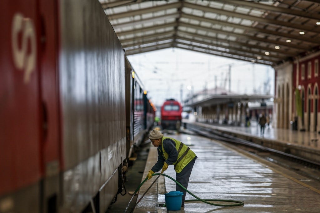 Una mujer limpia las vías mientras los trenes están estacionados en la estación de Santa Apolonia durante una huelga general en Lisboa el 11 de diciembre de 2025. (Foto de PATRICIA DE MELO MOREIRA / AFP)