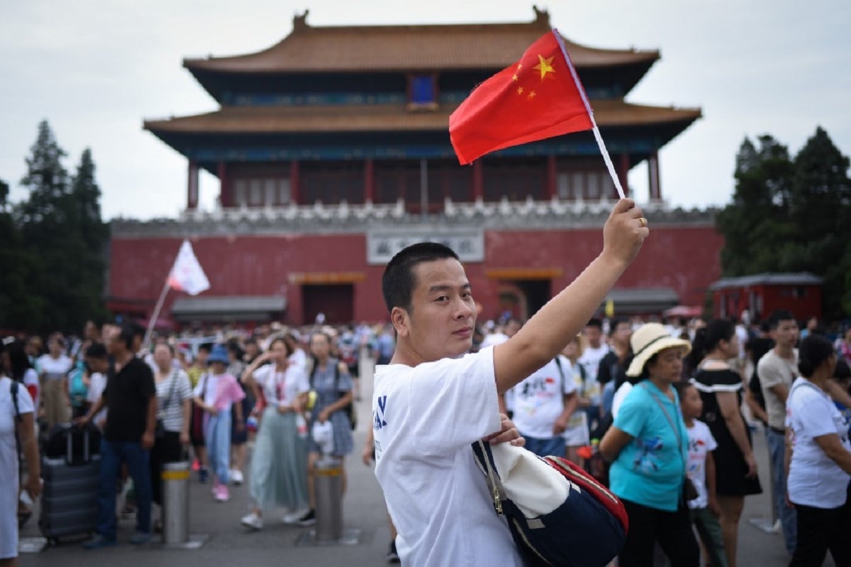 A man holding Chinese flags walks past the Forbidden City in Beijing on August 22, 2018. (Photo by WANG ZHAO / AFP)