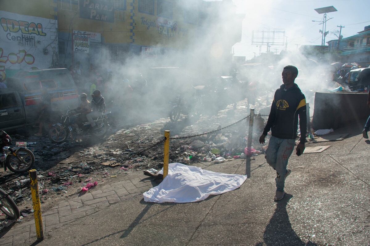 Un hombre pasa junto al cuerpo de una persona que estaba entre una docena asesinada en la calle por pandilleros, en Petionville, Puerto Príncipe, Haití, el 18 de marzo de 2024. (Foto de Clarens SIFFROY / AFP)