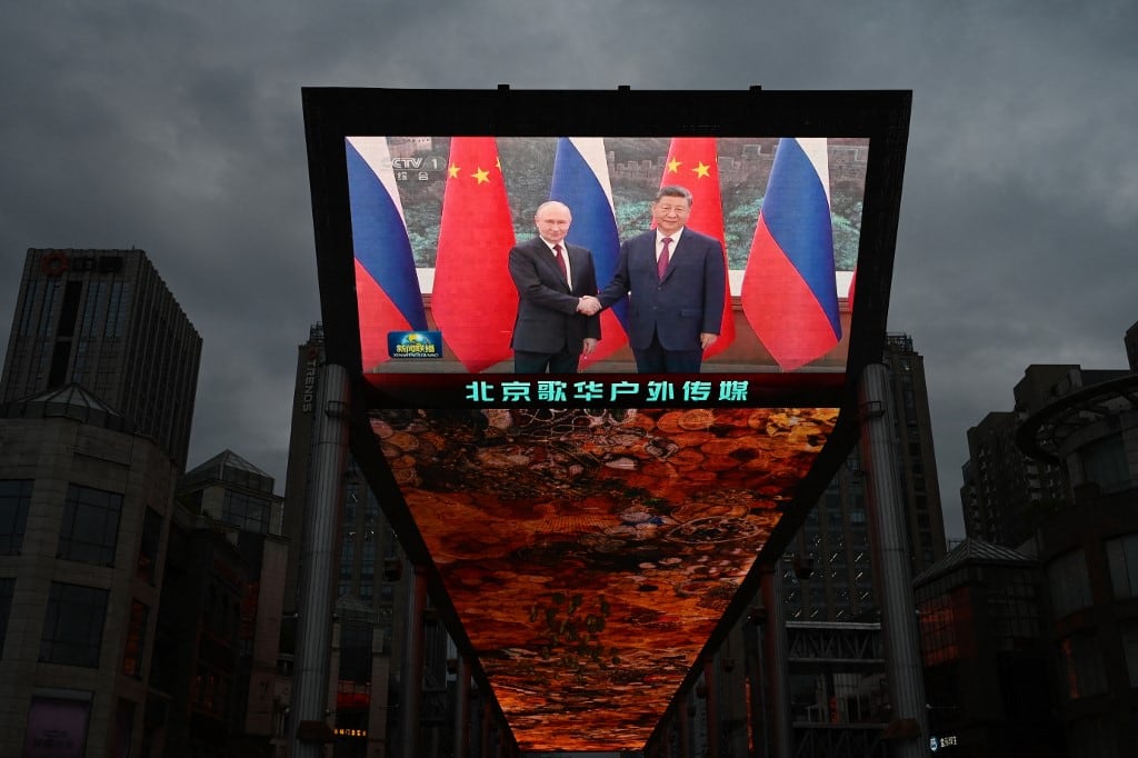 Un noticiero en una pantalla gigante a las afueras de un centro comercial muestra al presidente chino Xi Jinping (derecha) estrechando la mano del presidente ruso Vladimir Putin durante una reunión en Pekín el 20 de mayo de 2026. (Foto de GREG BAKER / AFP)