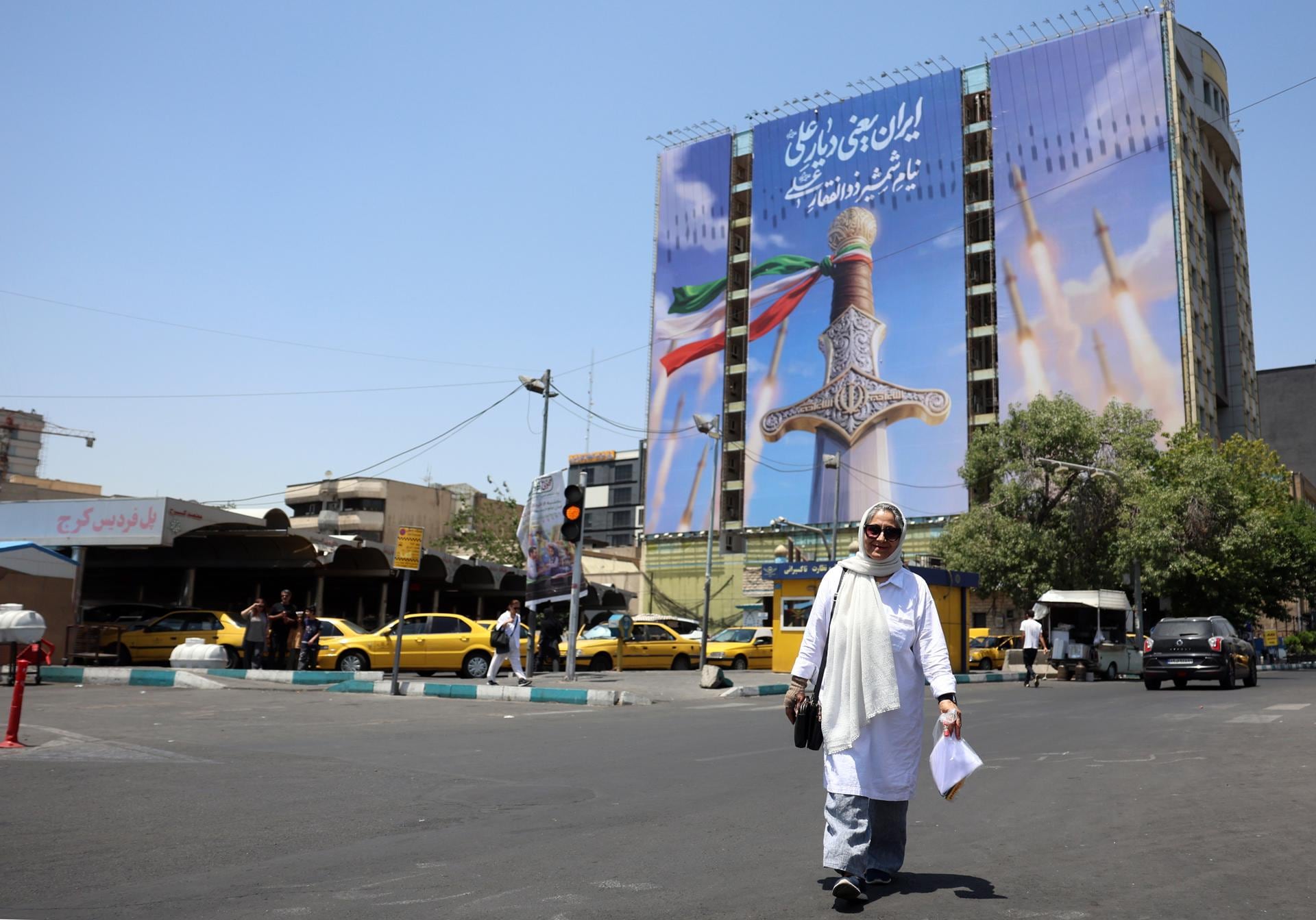 Ciudadanos iraníes pasan junto a una valla publicitaria política de gran tamaño con misiles de Irán y una espada en la plaza Vanak de Teherán, el 11 de junio de 2026. (EFE/EPA/ABEDIN TAHERKENAREH).
