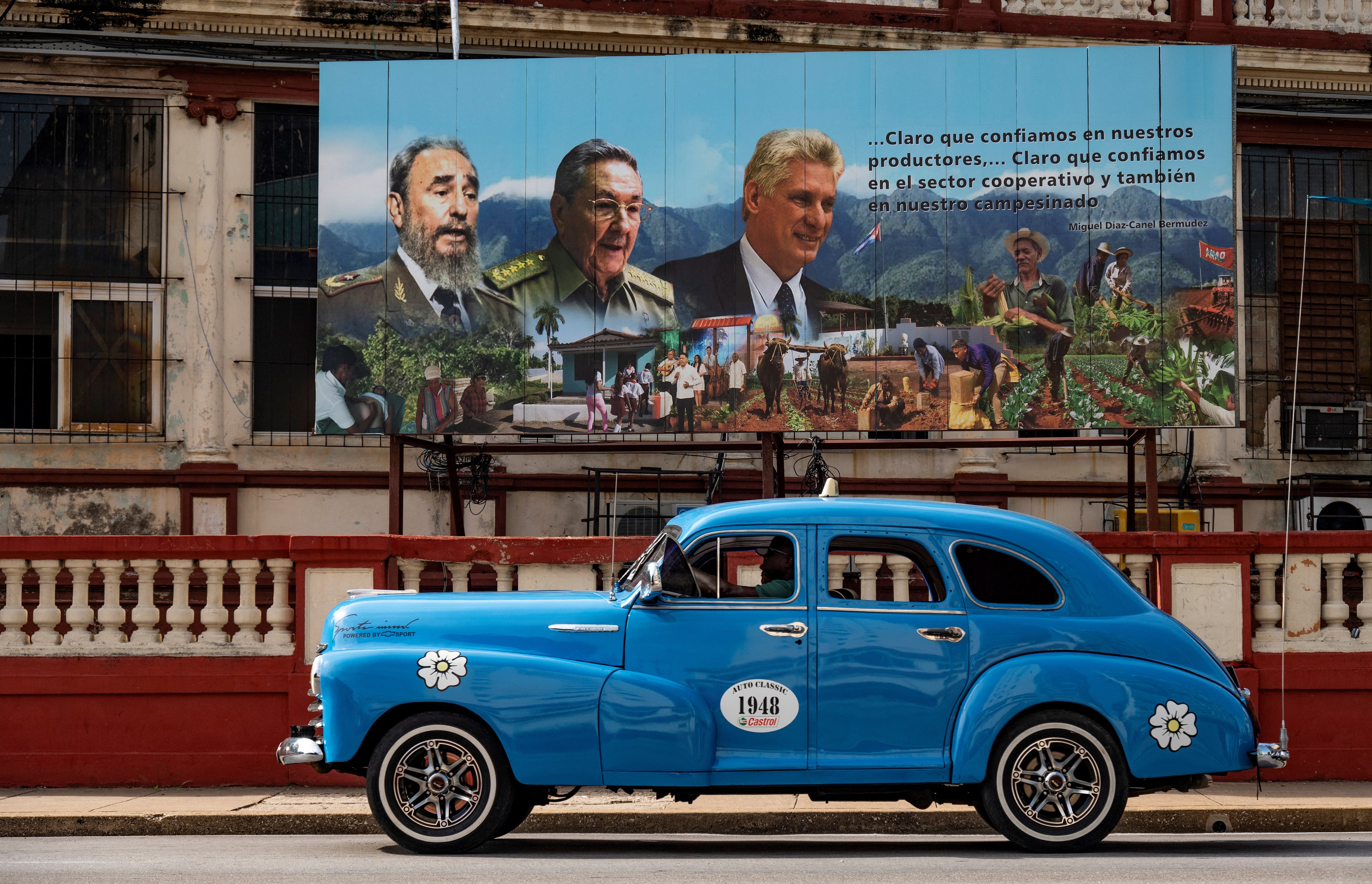 Un viejo automóvil estadounidense pasa cerca de un cartel del difunto líder cubano Fidel Castro, el ex presidente Raúl Castro y el actual presidente Miguel Díaz-Canel en La Habana, el 17 de agosto de 2023. (Foto de YAMIL LAGE / AFP).