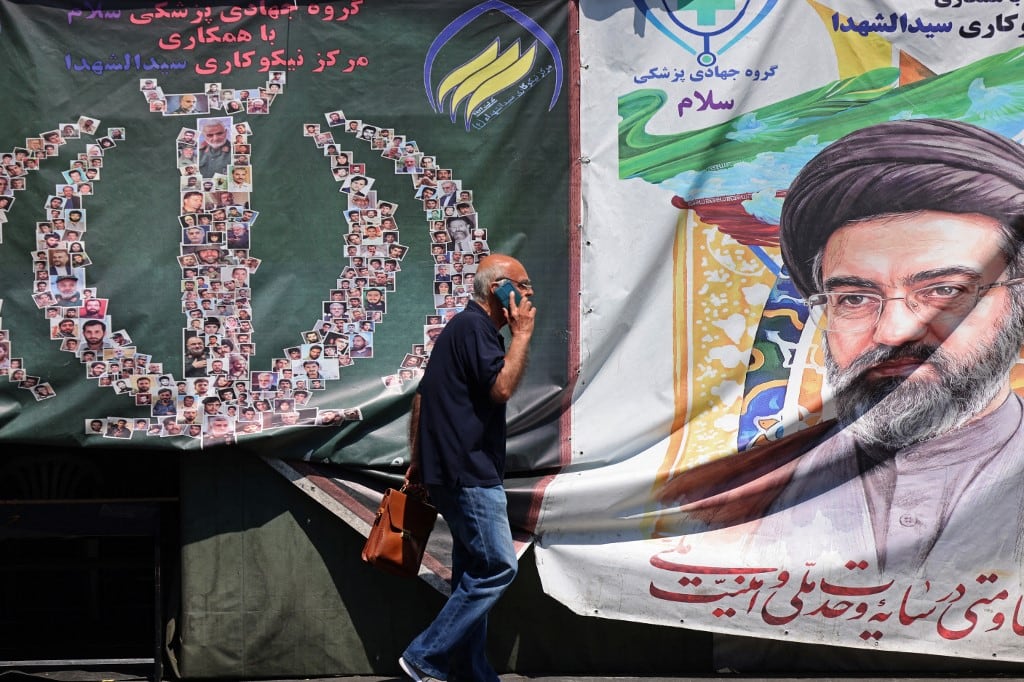 A man walks past a banner installed along the roadside of Iran's supreme leader Ayatollah Mojtaba Khamenei, in Tehran on April 29, 2026. US President Donald Trump on April 29 warned Iran to "better get smart soon" as efforts by Washington and Tehran to end hostilities appeared at a standstill. (Photo by ATTA KENARE / AFP) /