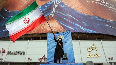 Una mujer ondea una bandera iraní frente a una valla publicitaria antiestadounidense que hace referencia al presidente de Estados Unidos, Donald Trump, y al estrecho de Ormuz en la plaza Valiasr de Teherán, el 5 de mayo de 2026. (Foto de AFP).