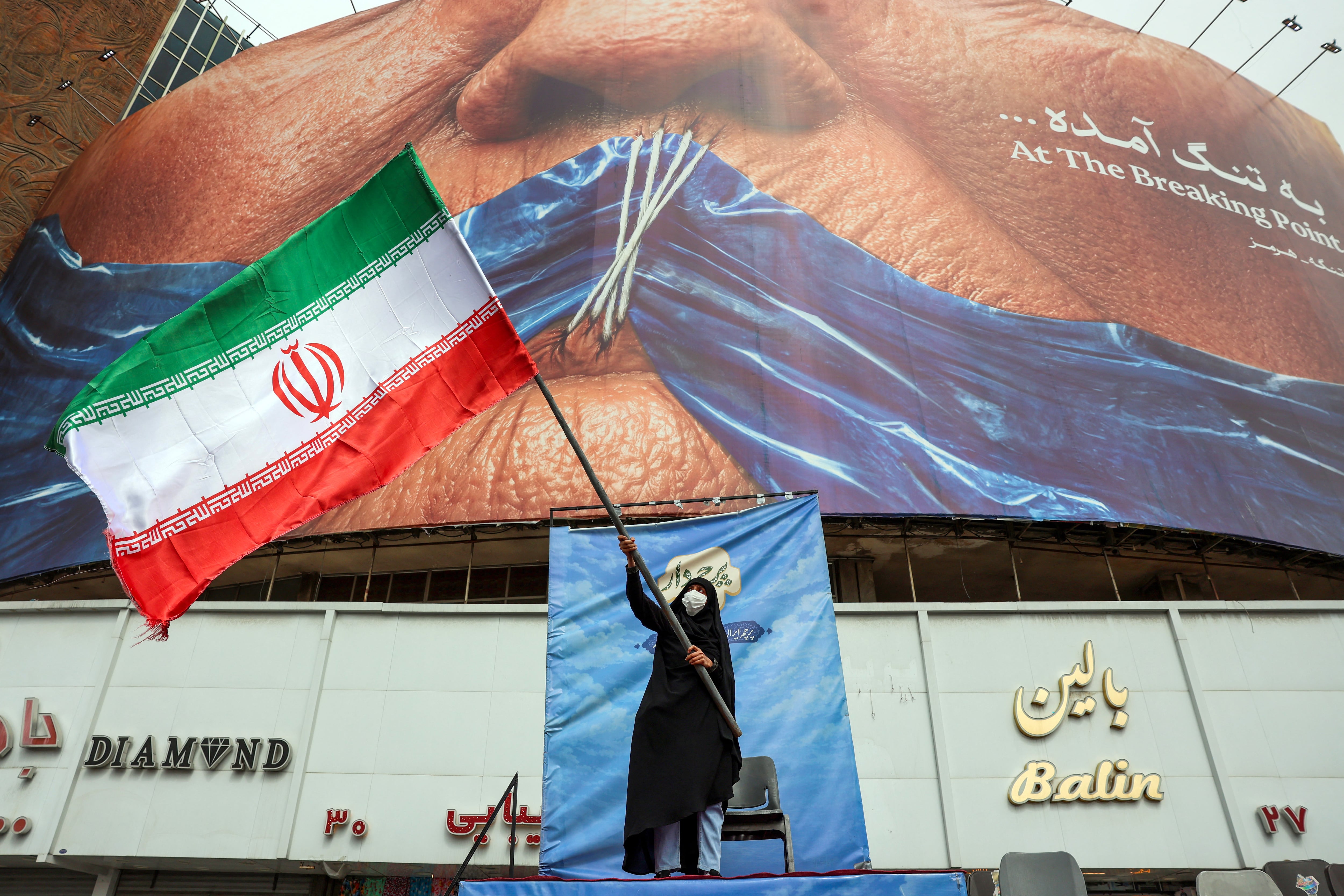 Una mujer ondea una bandera iraní frente a una valla publicitaria antiestadounidense que hace referencia al presidente de Estados Unidos, Donald Trump, y al estrecho de Ormuz en la plaza Valiasr de Teherán, el 5 de mayo de 2026. (Foto de AFP).