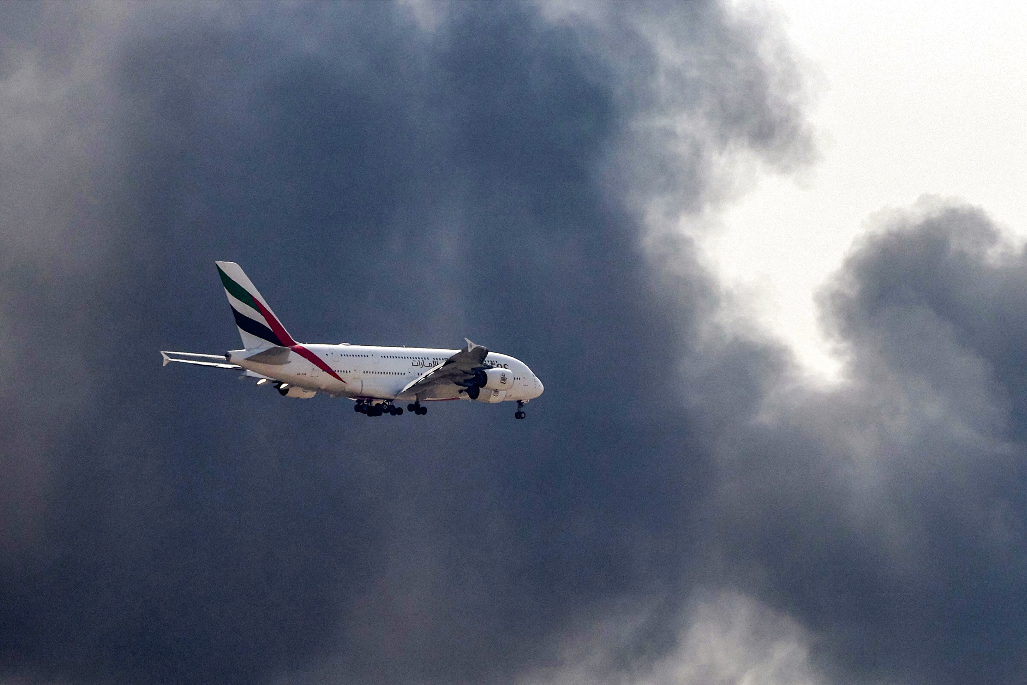 Un avión Airbus A380 de Emirates se prepara para aterrizar mientras una columna de humo se eleva desde un incendio en curso cerca del Aeropuerto Internacional de Dubái el 16 de marzo de 2026. (Foto de AFP).