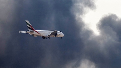 Un avión Airbus A380 de Emirates se prepara para aterrizar mientras una columna de humo se eleva desde un incendio en curso cerca del Aeropuerto Internacional de Dubái el 16 de marzo de 2026. (Foto de AFP).