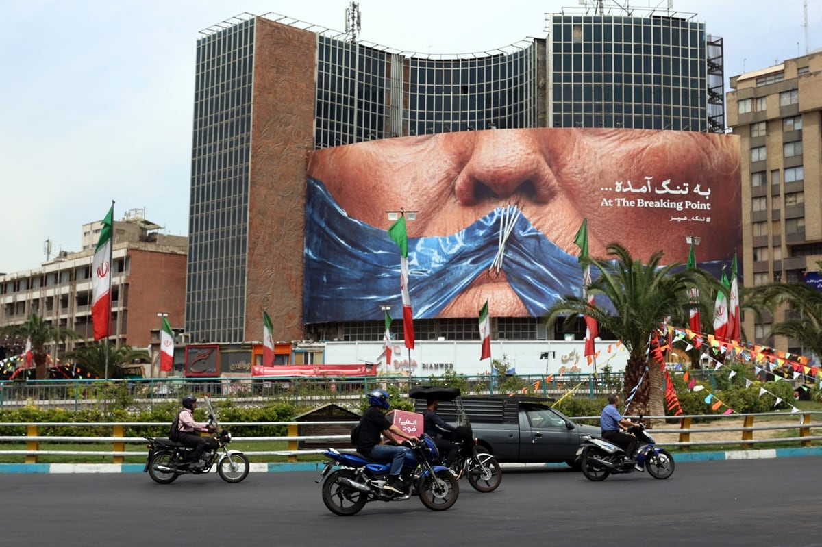 Iraníes pasaron en coche junto a una valla publicitaria que mostraba al presidente estadounidense Donald Trump y el estrecho de Ormuz, erigida en la plaza Valiasr de Teherán, el 28 de mayo de 2026. (AFP)