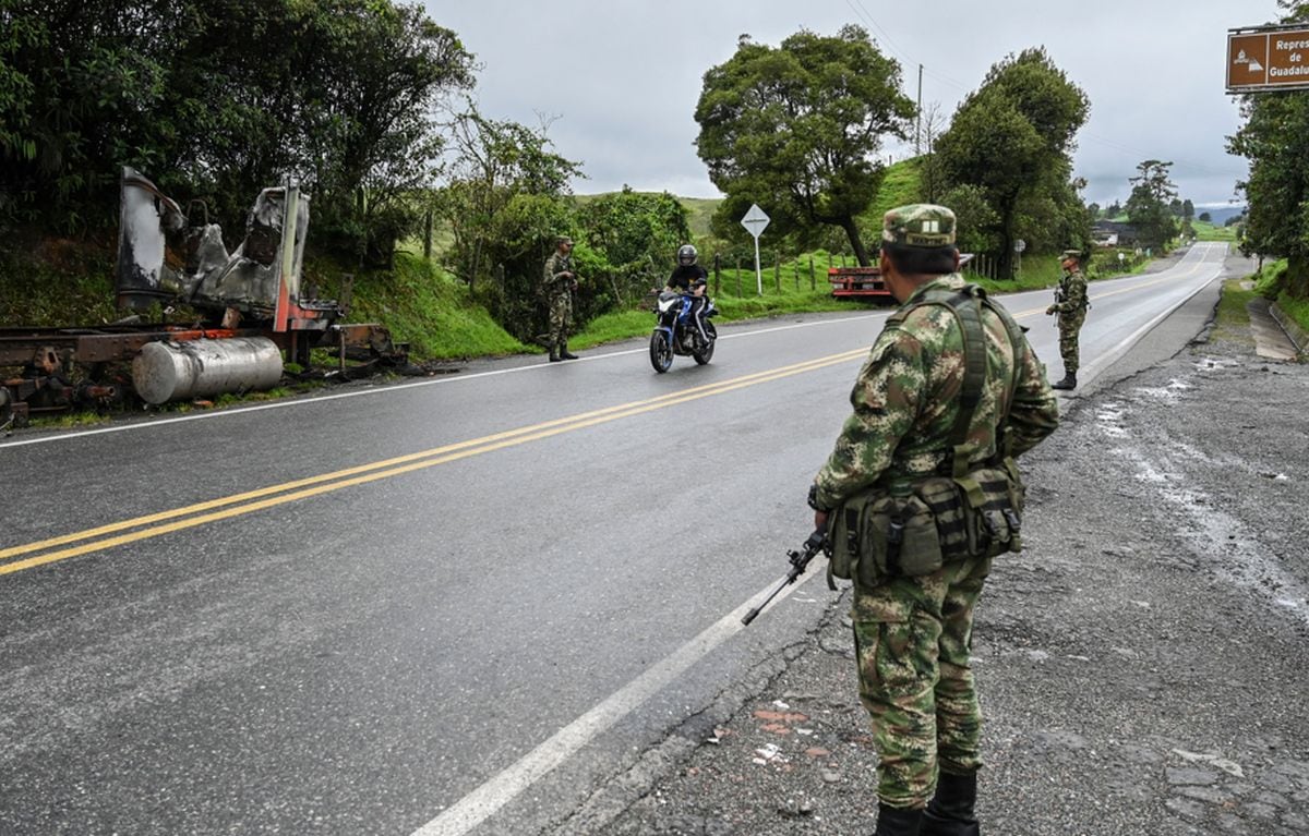 Imagen referencial y de archivo que muestra a soldados hacer guardia junto a un camión quemado por miembros del cartel de la droga Clan del Golfo, en una carretera cerca de Yarumal, departamento de Antioquia, Colombia, el 6 de mayo de 2022 | Foto: JOAQUIN SARMIENTO / AFP