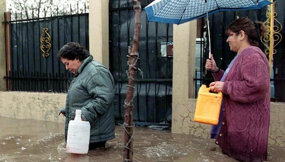Dos mujeres intentan avanzar por una calle inundada el 14 de junio de 2000 en Santiago, que fue declarada zona de desastre después de que fuertes lluvias paralizaran la capital y varias otras ciudades de Chile (Foto: Víctor Rojas / AFP)