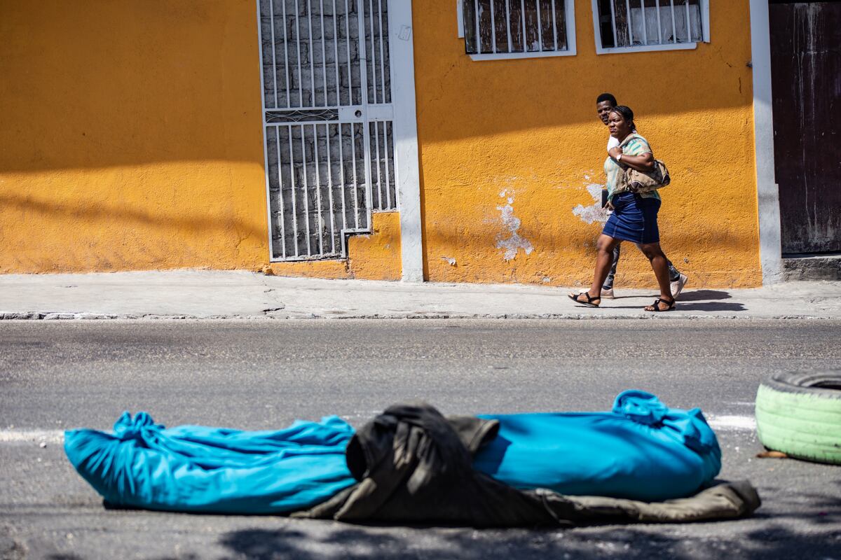 Dos personas caminan cerca de un cadáver de una persona en una calle de Petion-ville, en Puerto Príncipe, Haití, el 20 de marzo de 2024. (Foto de Mentor David Lorens / EFE)