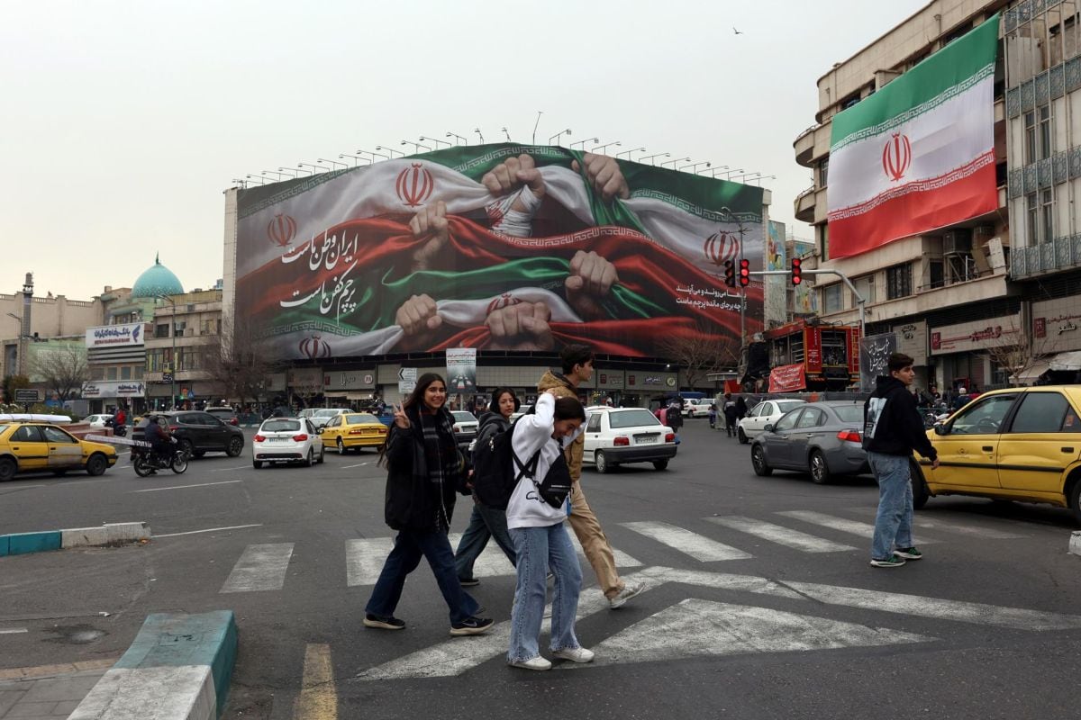 Jóvenes iraníes caminan junto a una valla publicitaria con el lema «Irán es nuestra patria» en la plaza Enqelab de Teherán, Irán, el 13 de enero de 2026. Foto: EFE/EPA/ABEDIN TAHERKENAREH