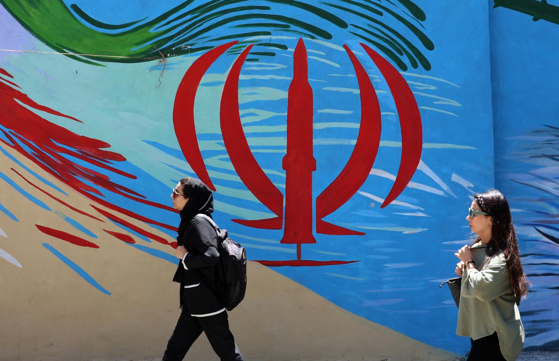 Mujeres pasan junto a un mural con la bandera nacional de Irán en una calle de Teherán el 15 de junio del 2026, tras el acuerdo de paz con Estados Unidos. (EFE/EPA/ABEDIN TAHERKENAREH).