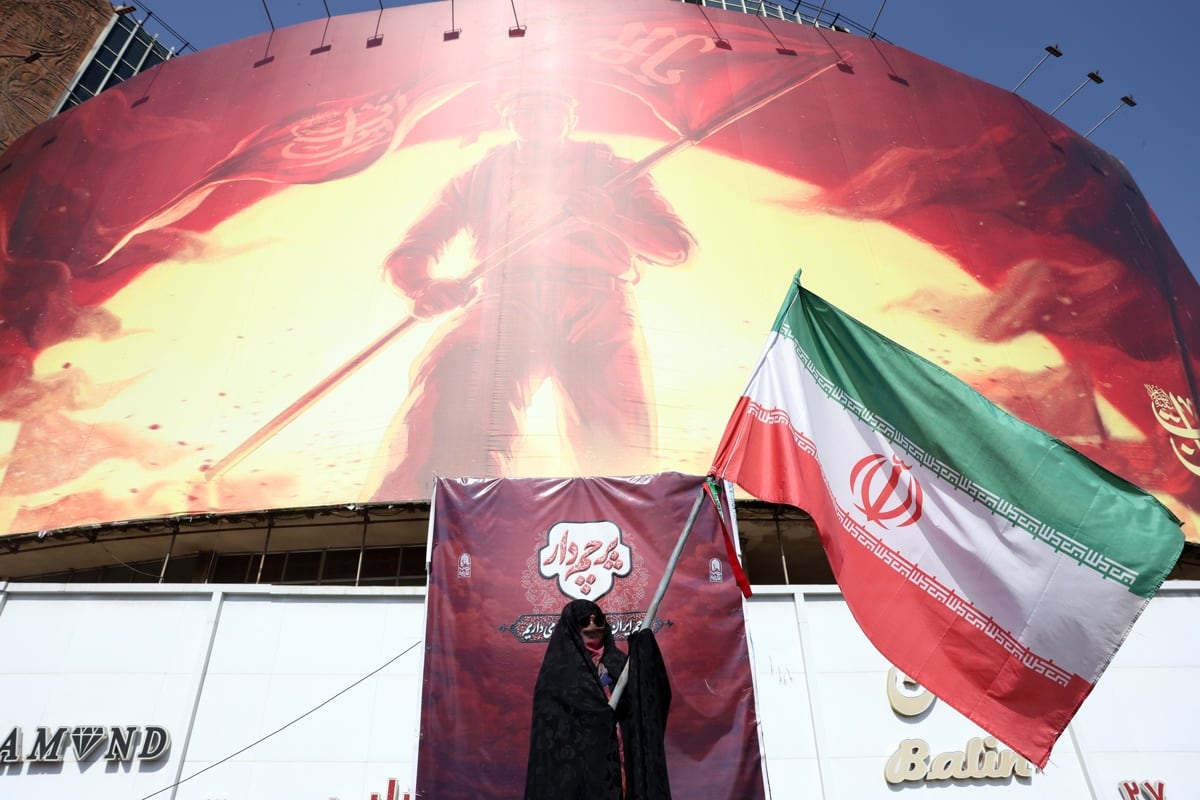 Una mujer iraní sostiene la bandera nacional de Irán frente a una valla publicitaria política en la plaza Valiasr, en el centro de Teherán, Irán, el 13 de septiembre de 2026. (EFE/EPA/ABEDIN TAHERKENAREH)
