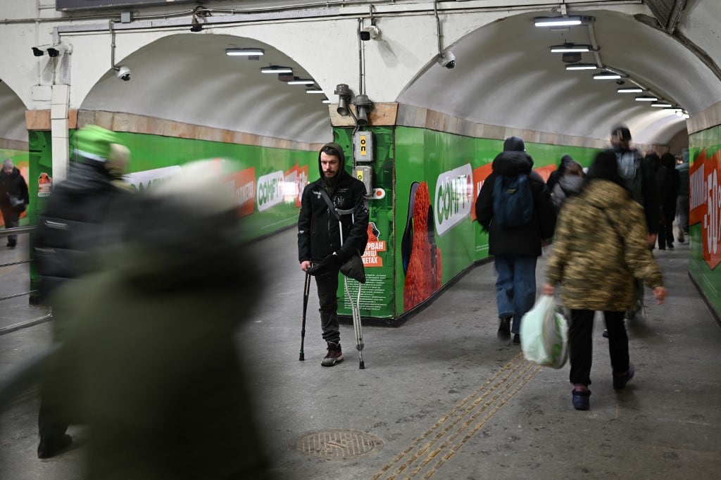 Unos peatones pasan junto a un amputado que pide limosna en una estación de metro durante una alerta antiaérea en Kiev el 26 de enero de 2026, en plena invasión rusa de Ucrania. (Foto de Sergei GAPON / AFP)