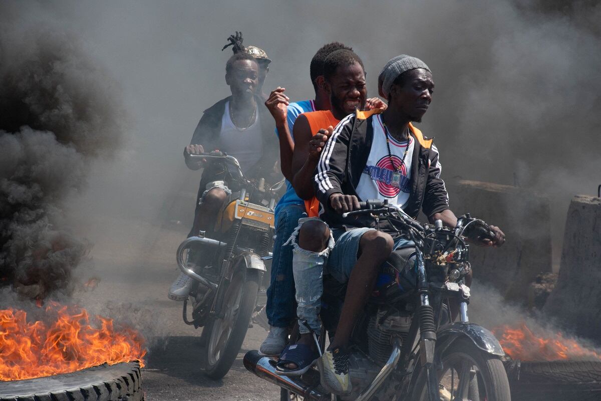 Hombres en motocicletas pasan quemando neumáticos durante una manifestación tras la dimisión de su primer ministro Ariel Henry, en Puerto Príncipe, Haití, el 12 de marzo de 2024. (Foto de Clarens SIFFROY / AFP)