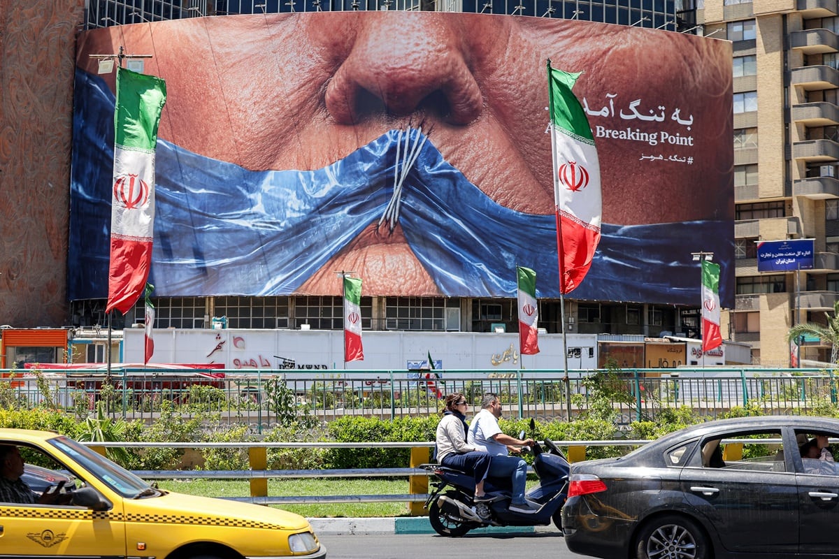 Varios automovilistas circulan con sus vehículos junto a una valla publicitaria política que muestra al presidente estadounidense Donald Trump y el estrecho de Ormuz en la plaza Valiasr de Teherán, el 26 de mayo de 2026. (ATTA KENARE / AFP) /
