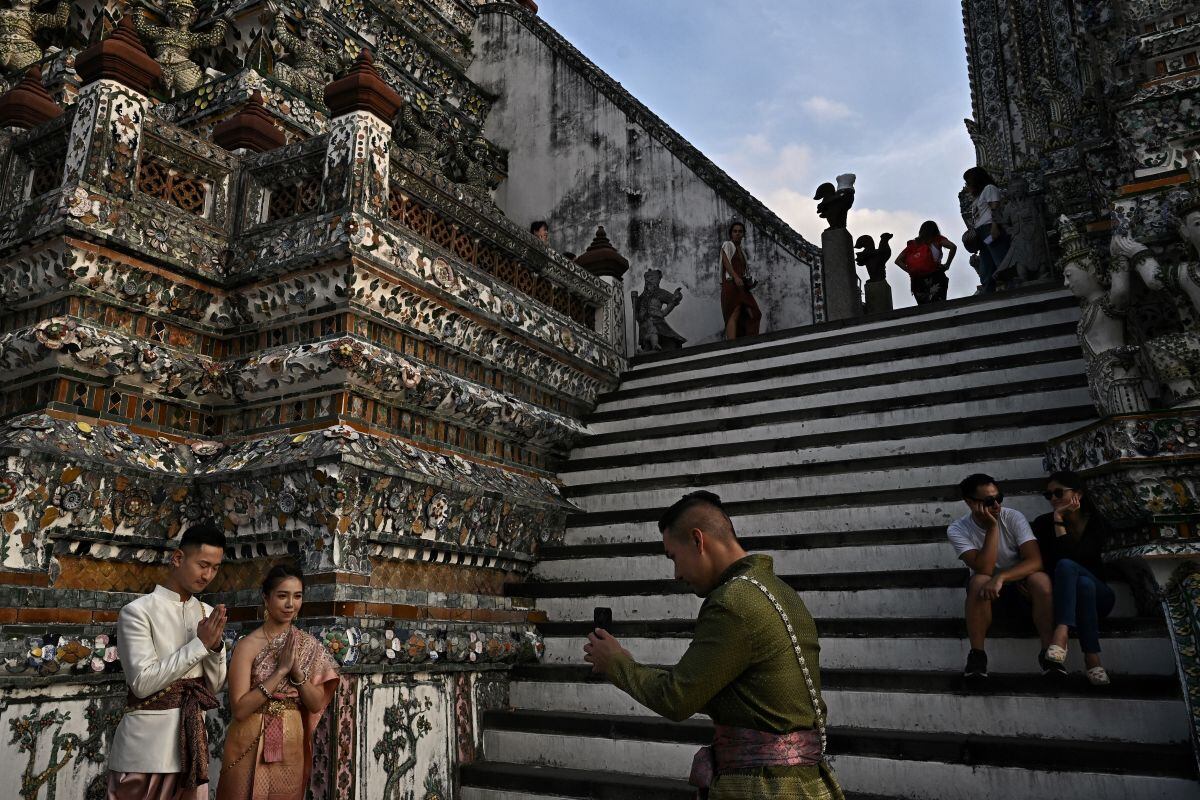Turistas con trajes tradicionales tailandeses toman fotografías en el templo budista Wat Arun en Bangkok el 9 de diciembre de 2022. (Foto de Lillian SUWANRUMPHA / AFP)
